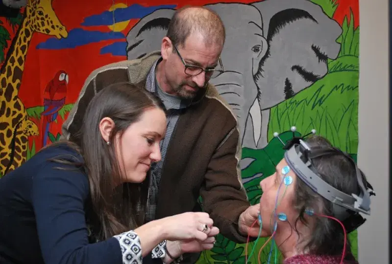 Two SFD Lab Researchers attach sensors to the head of a patient in front of a colorful painting of animals