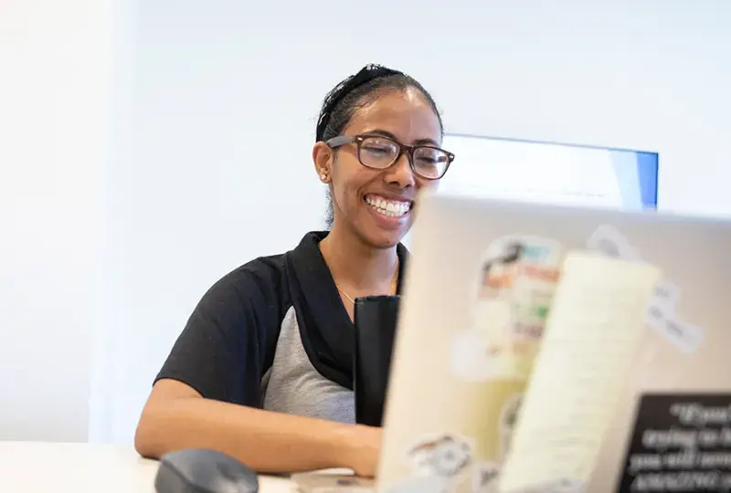 woman smiles and looks at her laptop which is covered with stickers