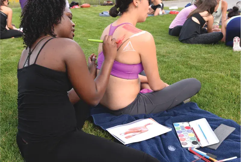 A woman drawing on another woman's back while wearing athletic clothing