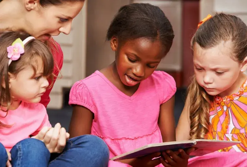 three little girls read a book together