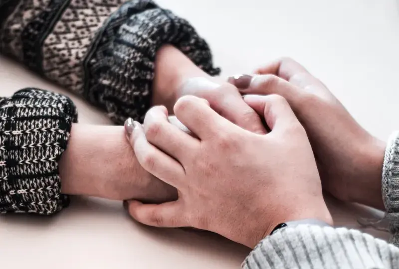 Hands of two people on a table, one person grasps the other's hands in a supportive gesture