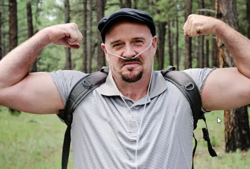 a man wearing an oxygen tube makes muscles with his arms in the woods
