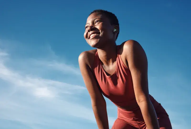 woman rests with hands on her knees, smiling. She wears workout gear.