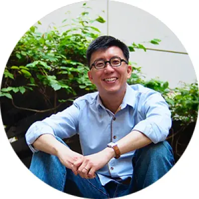 a man of Asian heritage sits in front of a green bush