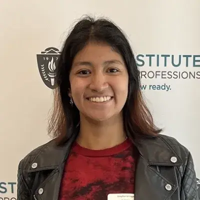 steph smiles in front of a banner that says MGH Institute she has dark brown shoulder length hair