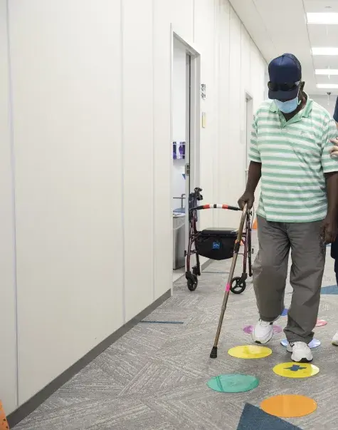 student assisting a client who has a cane to walk down the hall