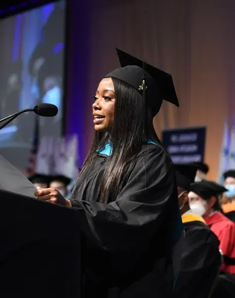ashley stands at a podium at graduation in her cap and gown