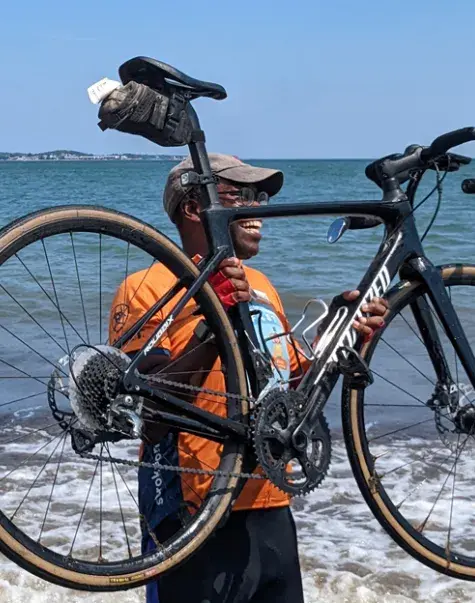 Obel-Omia holds his bike during the celebratory "wheel dip" in Revere, Massachusetts, marking the completion of the cross-country bike journey.