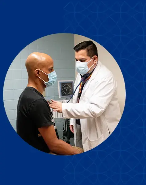 man in surgical mask listens to the heart of another man with a stethoscope