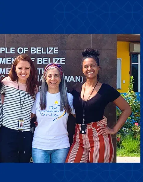 four women stand in front of a people of belize sign