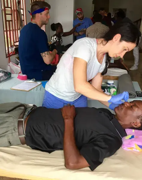 woman attends to a man's face who is lying in a hospital bed