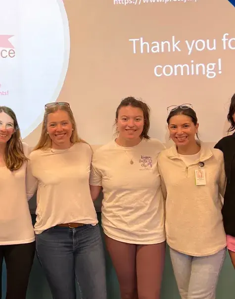 group of students in front of a projection that says thank you for coming with a pink cancer ribbon