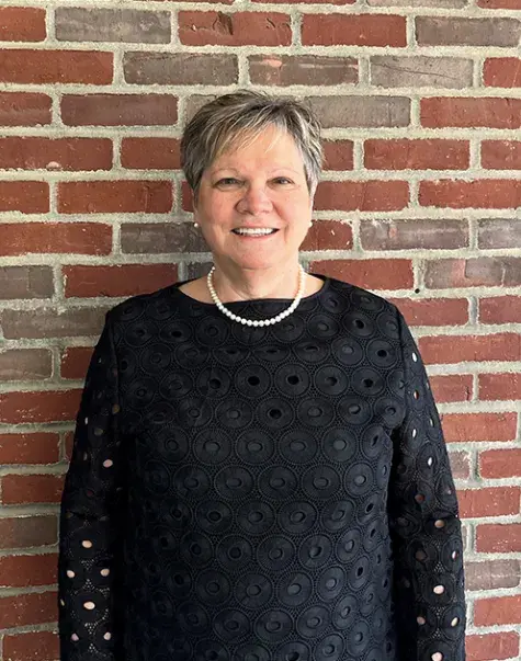 Doctor of Occupational Therapy program faculty member standing against a brick wall, smiling, and wearing a black blouse with a pearl necklace.