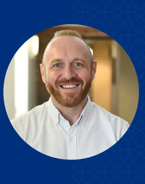 brad has a reddish brown beard and mustache and wears a white collared shirt