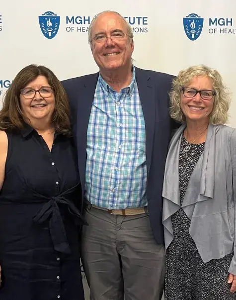 charley stands with his arms around the two ladies next to some silver balloons