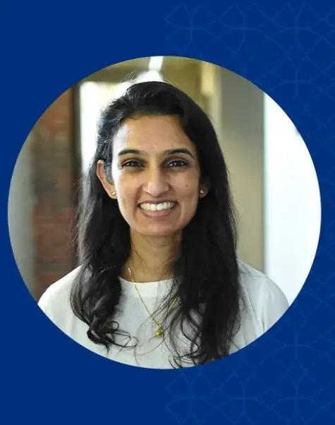 isha has shoulder length black hair and is wearing a gold chain and a cream long sleeve top