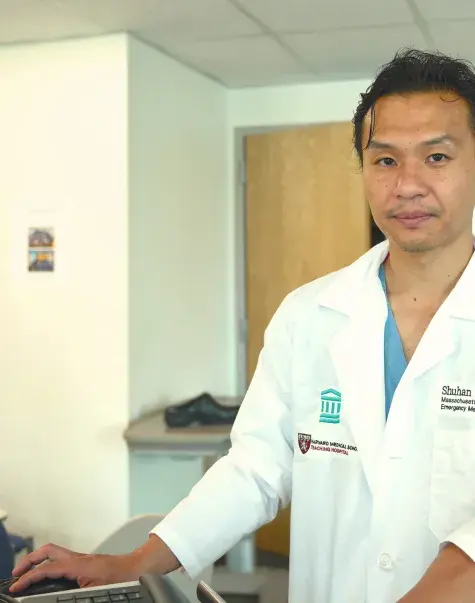 shuhan stands at a computer in a clinical office and wears a white coat 
