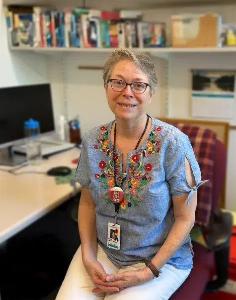 antonia has a brightly flower patterned blouse on and sits in an office chair