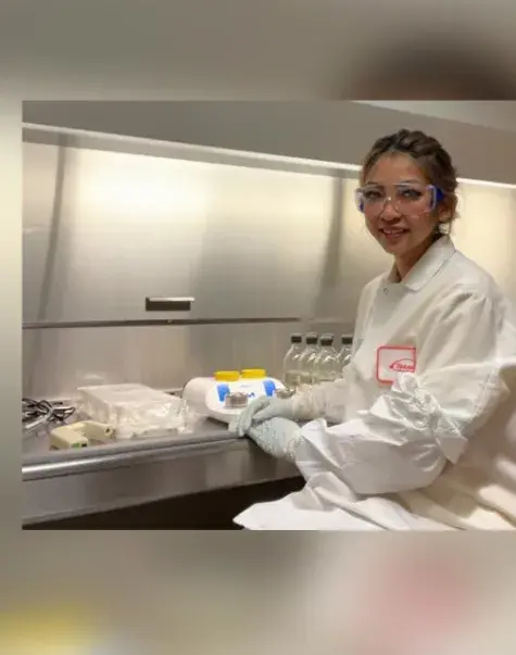 junny sits in a lab with a lab coat and lab glasses on