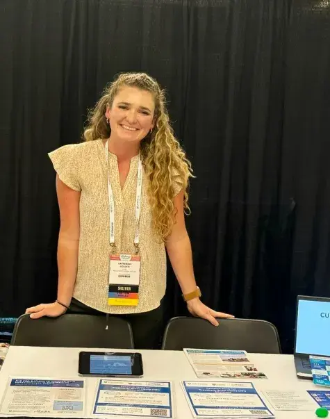 katie stands in front of a table full of papers at a conference