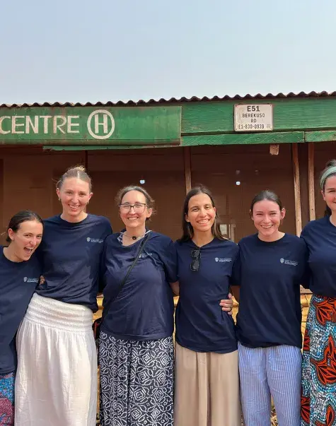 Seven women stand next to each other posing for a photo in front of a health center