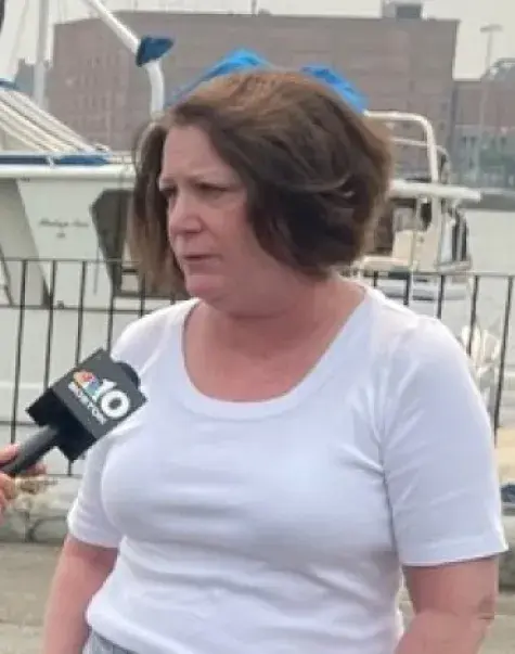 A women on the left holds a microphone with a camera behind her while another women speaks into the microphone