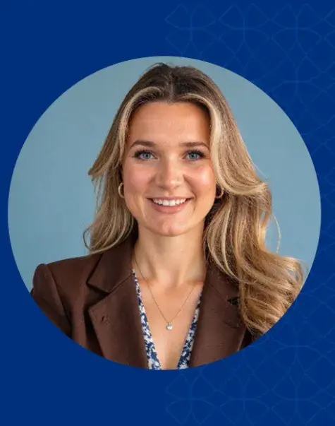 Woman with blonde hair smiling and wearing a brown jacket