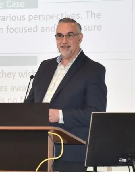 A man stands at a podium with a woman standing next to him and empty seats to his right