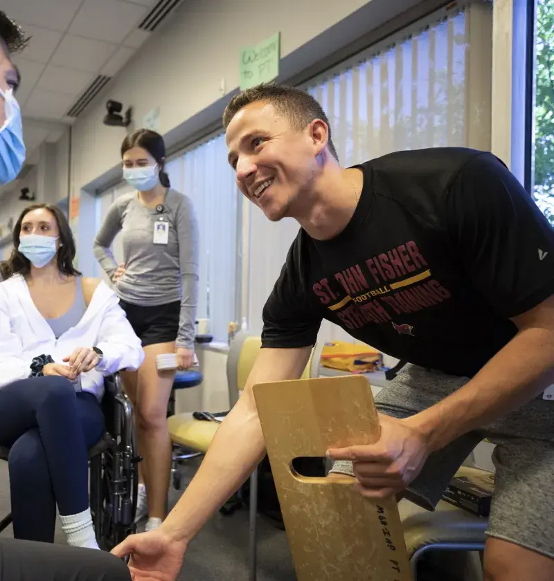 man holds wooden step and gestures to a knee while smiling