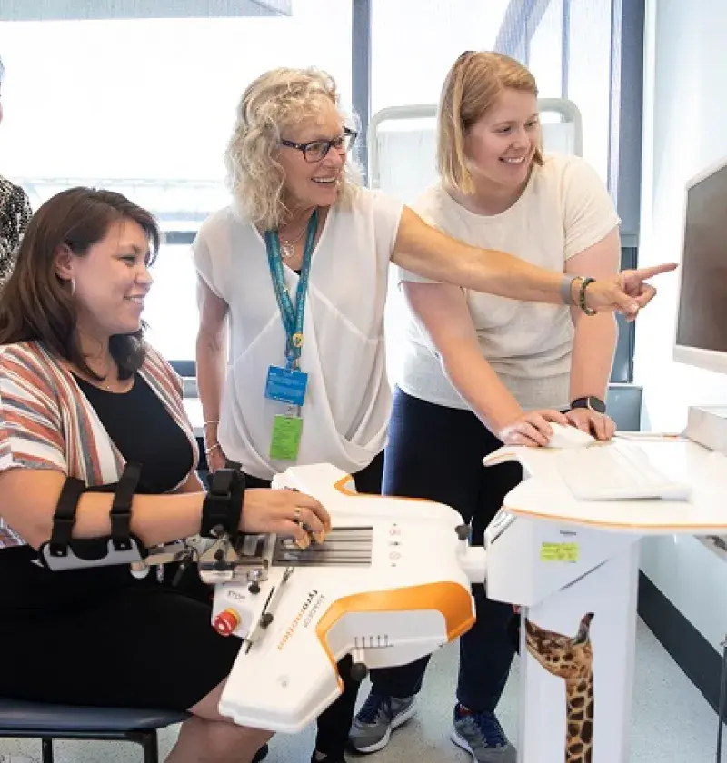 woman points to screen while others look on and one has her arm in the controls