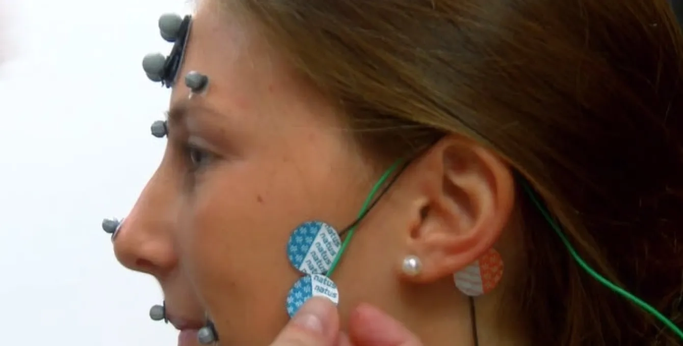 A brown-haired woman's head in profile has sensors placed under her temple and below her ear