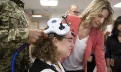 man holds device that looks like a big T to a woman's head while others look at a computer